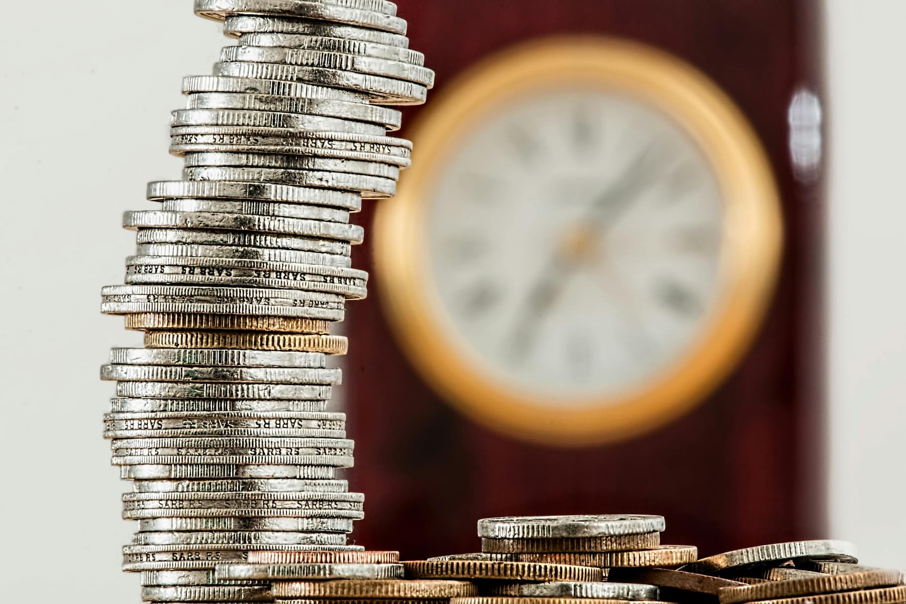 selective focus photo of stacked coins in front of a clock